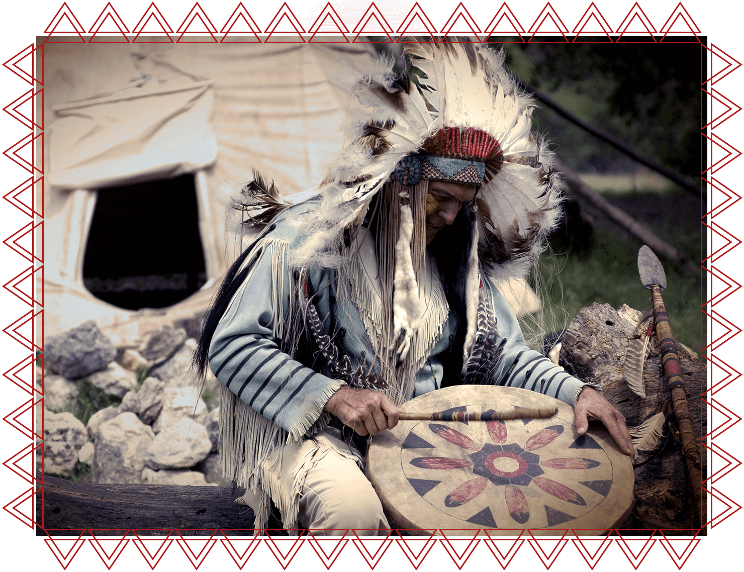 IACFS Schamanismus Akademie - Shaman Leader Lehrgang - Indigener Schamane mit Federhaupt sitzt vor Tipi und schlägt eine Trommel