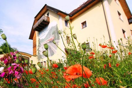 Rote Mohnblumen vor gelbem Haus mit Zug-Wandgemälde.